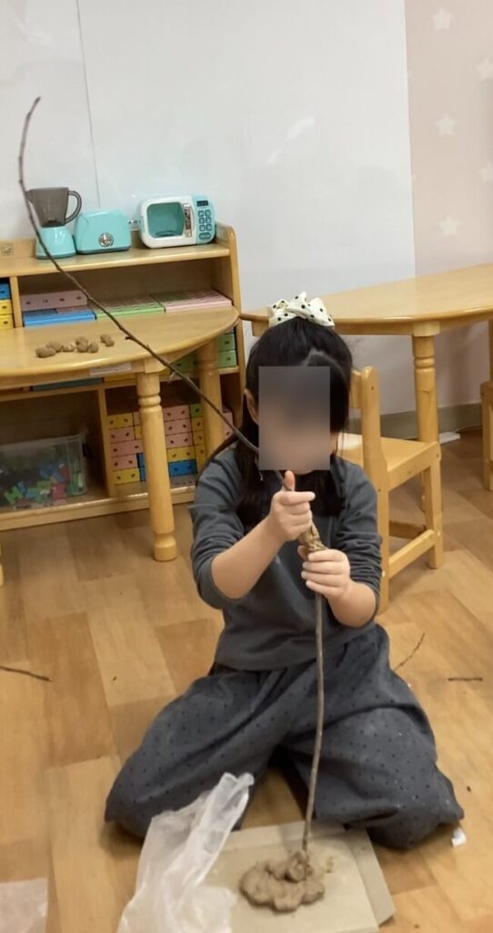 한 아이가 점토와 나뭇가지를 이용해 나무를 만들며 탐구하는 모습