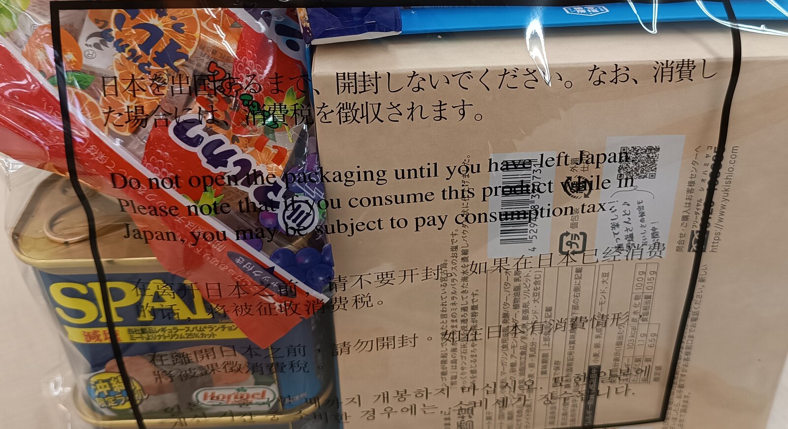 과자 봉지와 통조림, 상자가 든 투명한 비닐 밀봉 봉투. 봉투 겉면에 일본어·영어·중국어·한국어로 일본을 떠날 때까지 뜯지 말라는 문구가 인쇄되어 있다