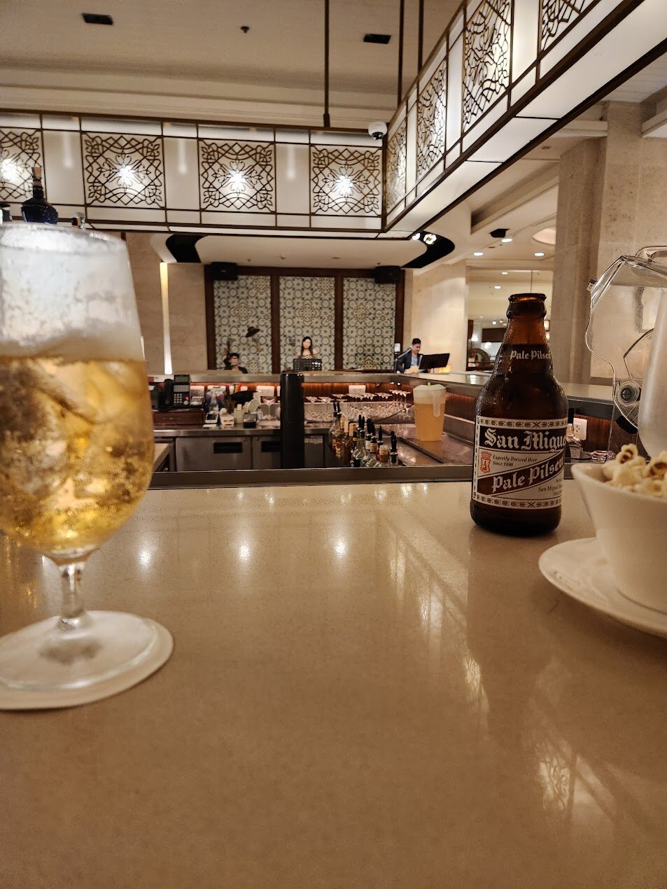 저녁 조명이 켜진 실내 바 카운터에 맥주병과 팝콘이 놓여 있고 뒤쪽 무대에서 밴드가 연주하는 모습